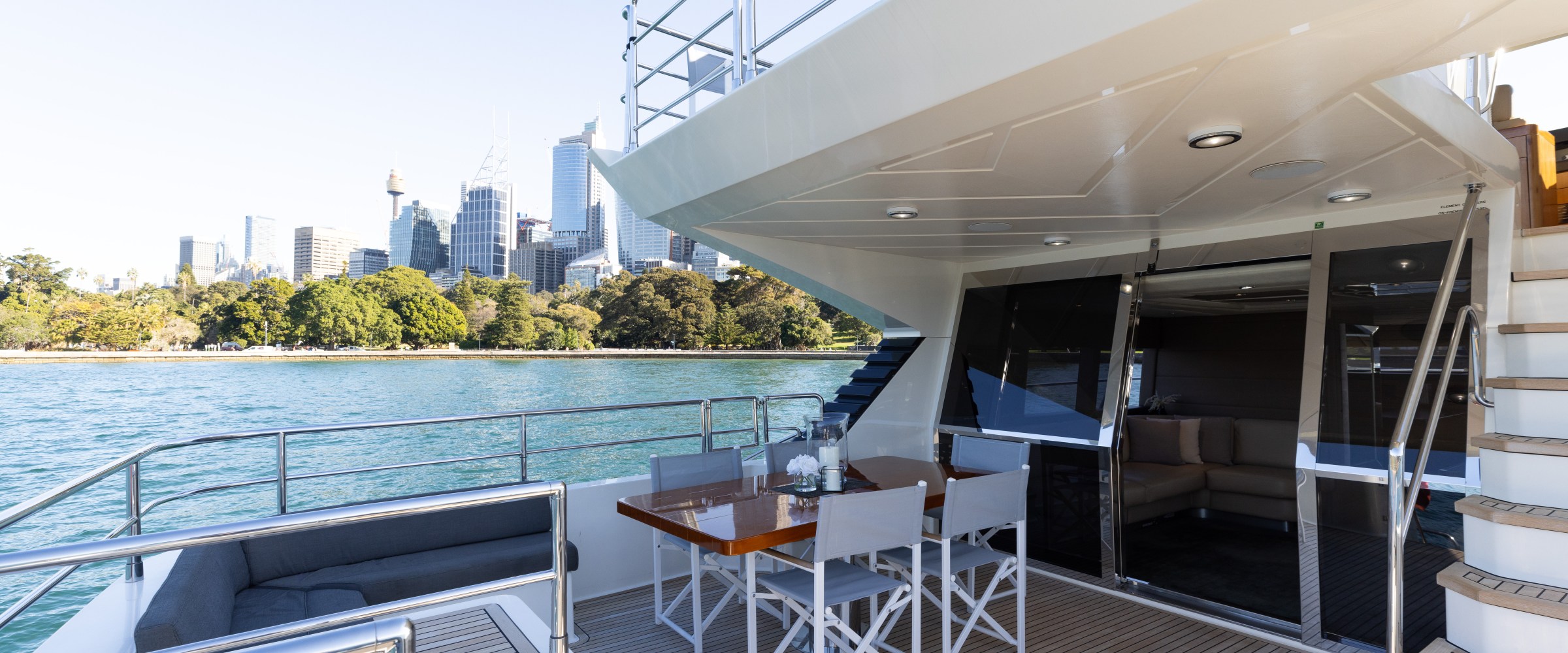 Luxury yacht deck with table, chairs, and city skyline in background.