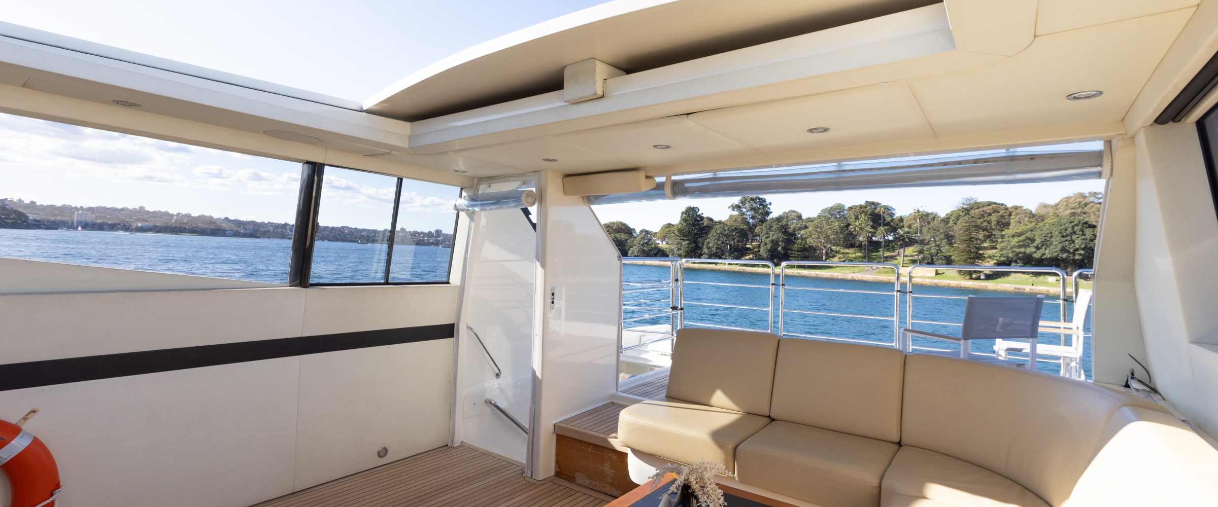 Luxury yacht deck with beige seating, table, and view of water and trees.