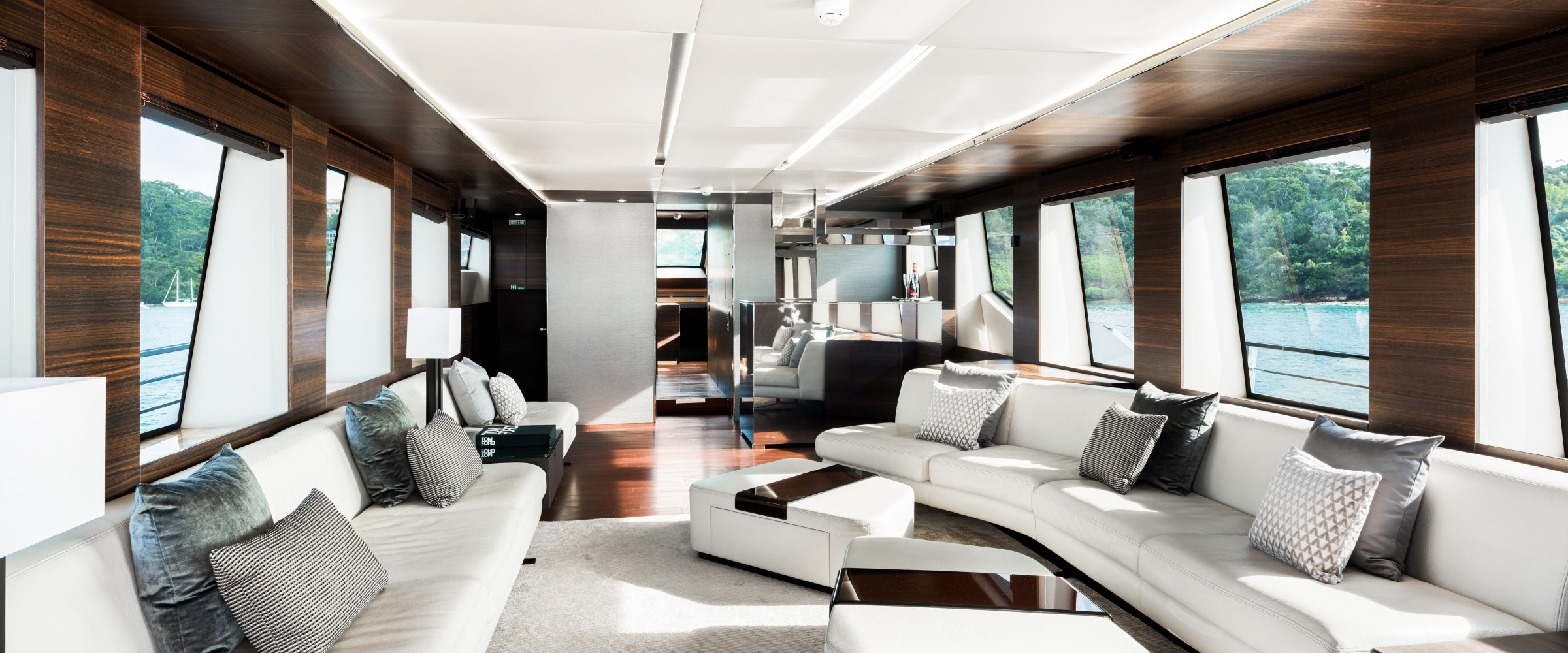 Luxurious yacht interior with white sofas, wooden accents, large windows, and a view of the sea.