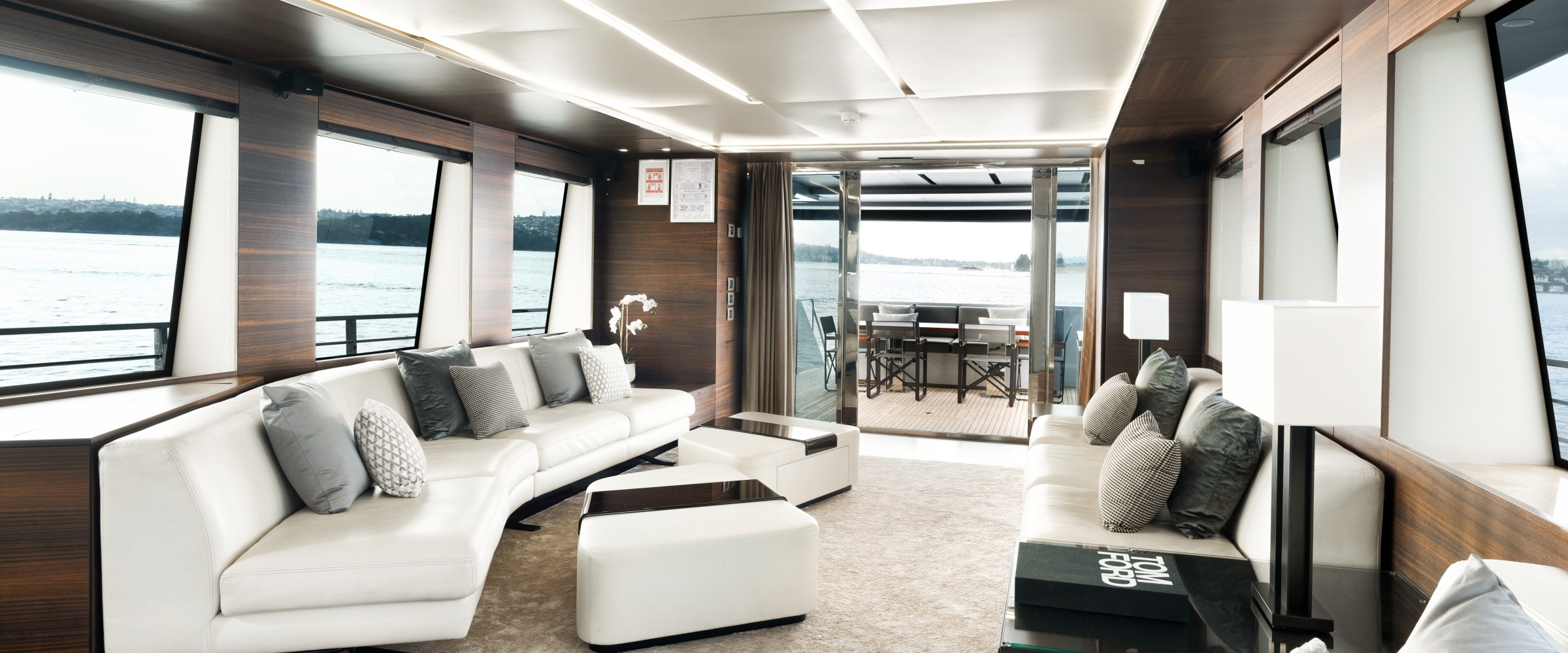 Luxurious yacht interior with white sofas, panoramic windows, and a view of the water outside.
