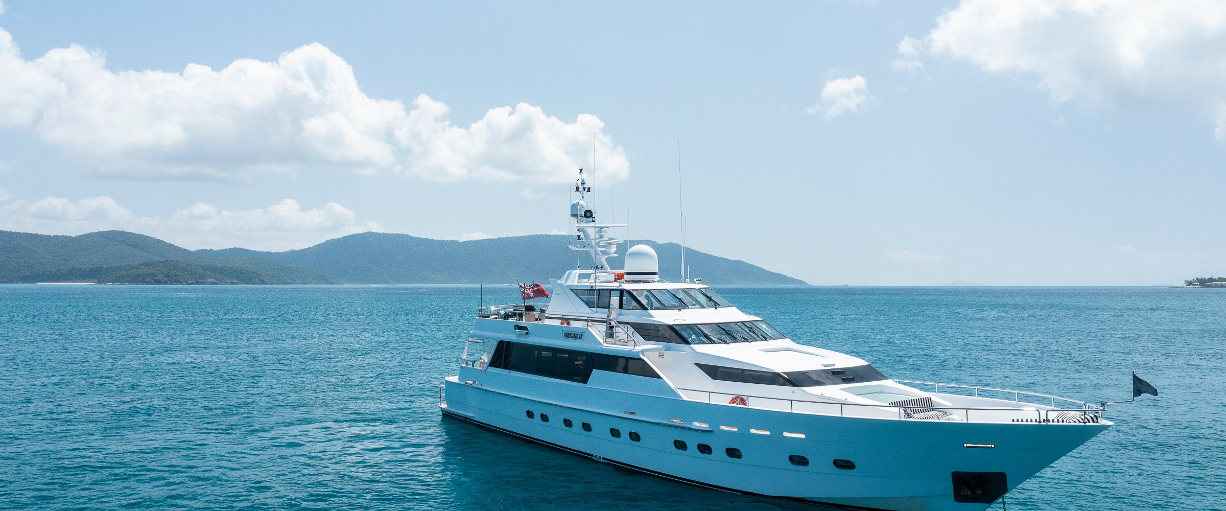 A luxury yacht on calm blue water with distant hills under a bright sky.