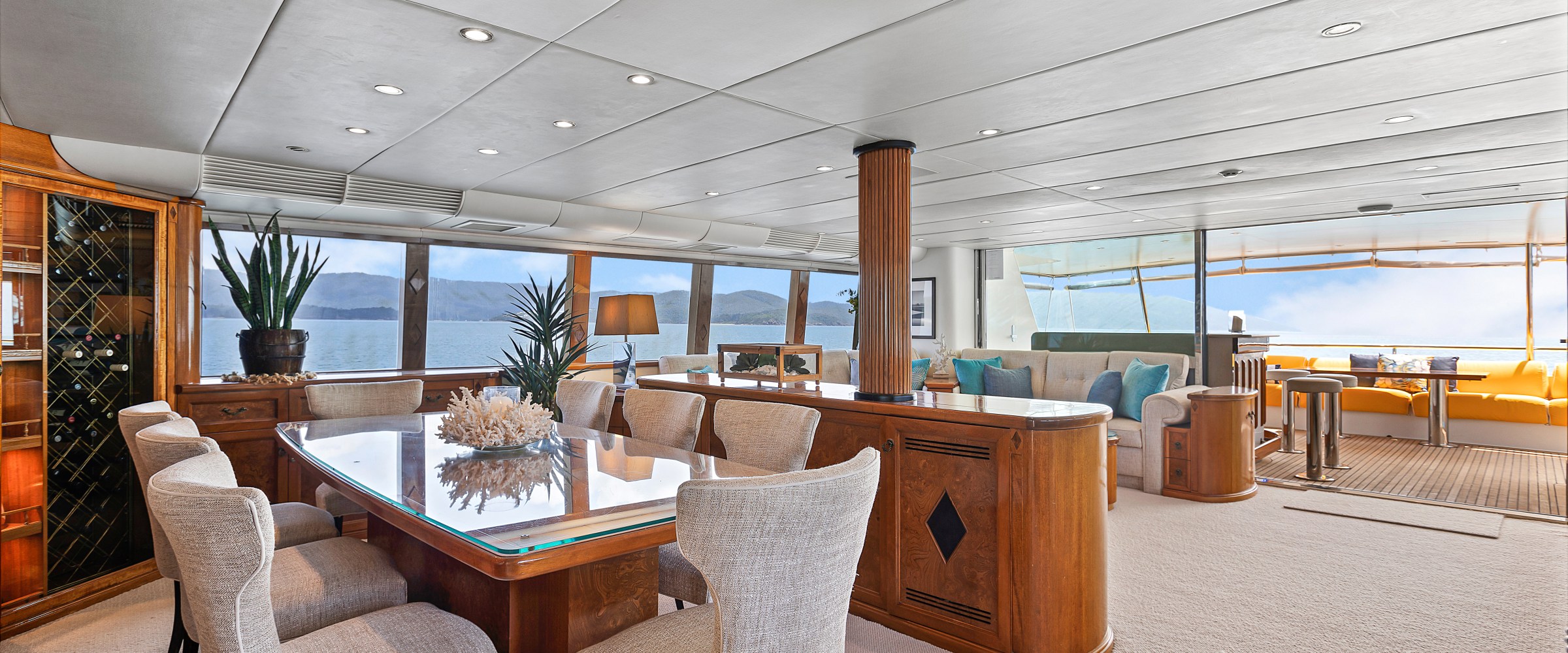 Luxurious yacht interior with a dining table, chairs, and large windows overlooking the ocean.