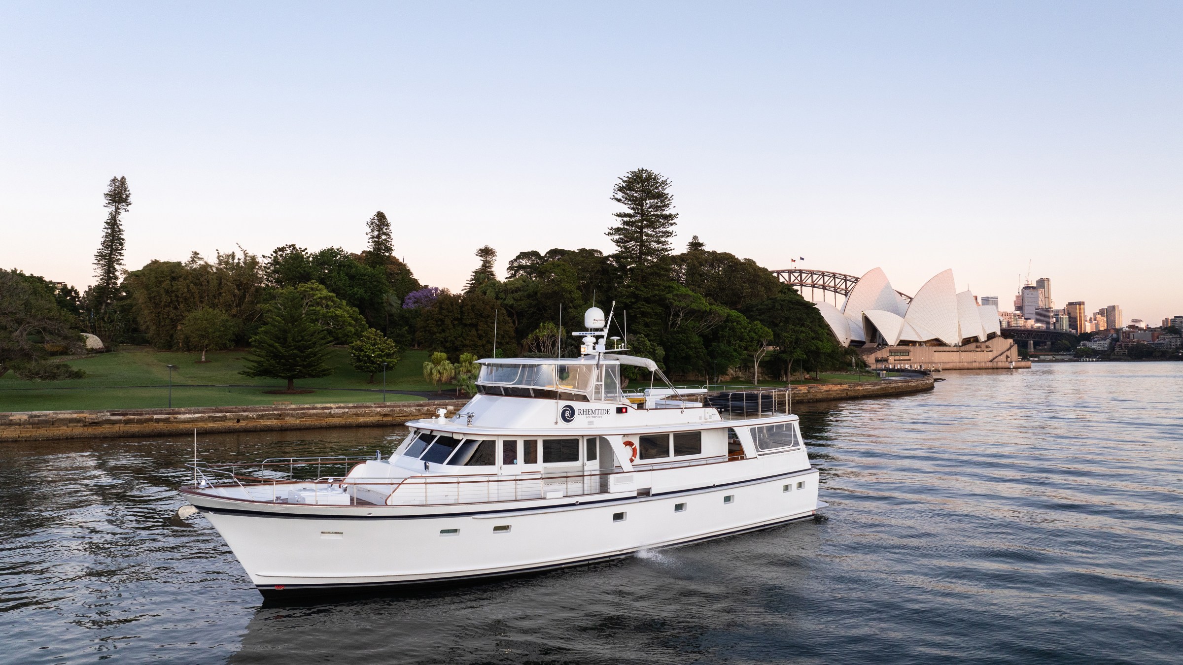 White yacht sailing near Sydney Opera House at sunset.