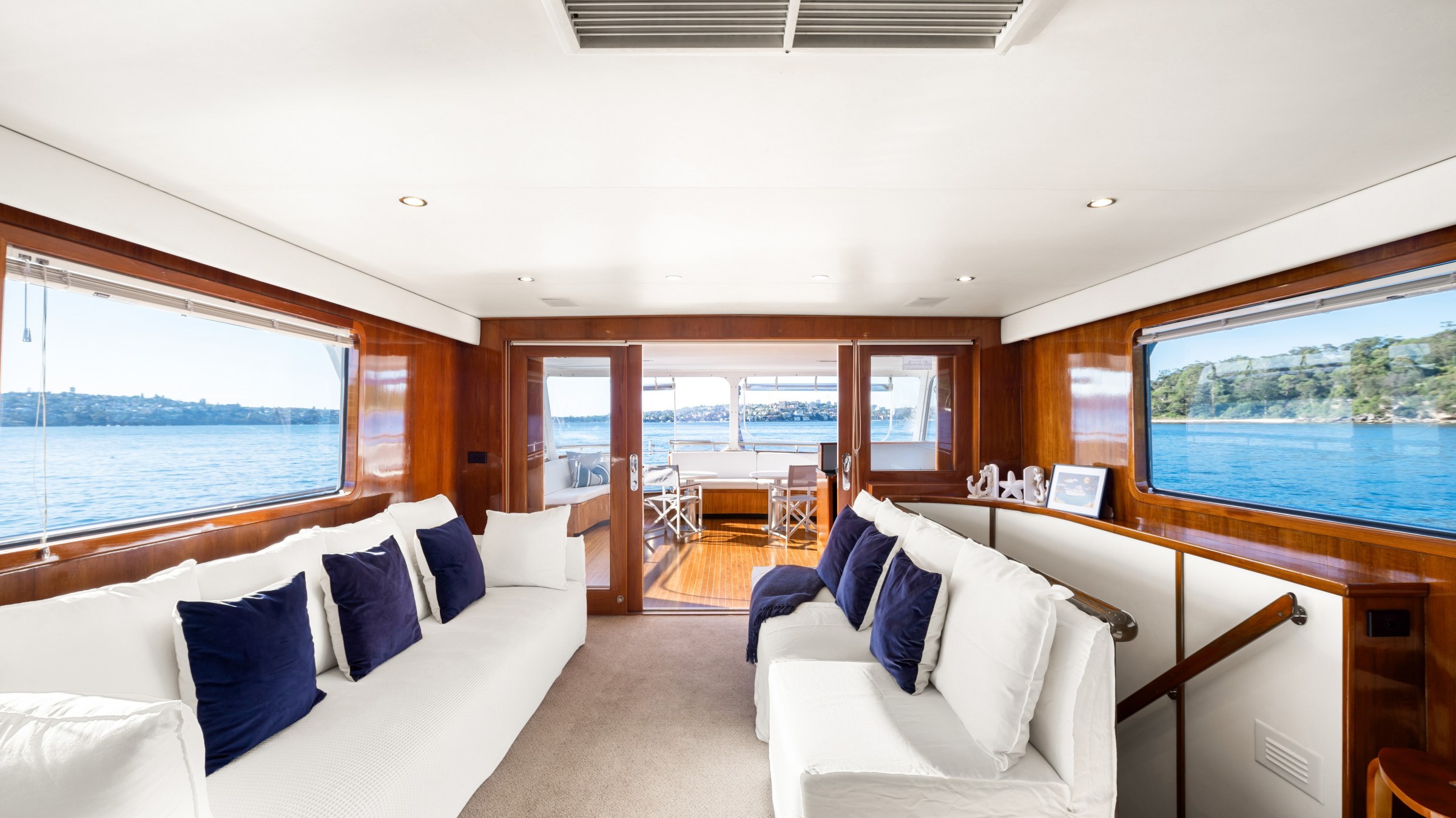 Luxurious yacht interior with white sofas, blue cushions, large windows, and sea view.