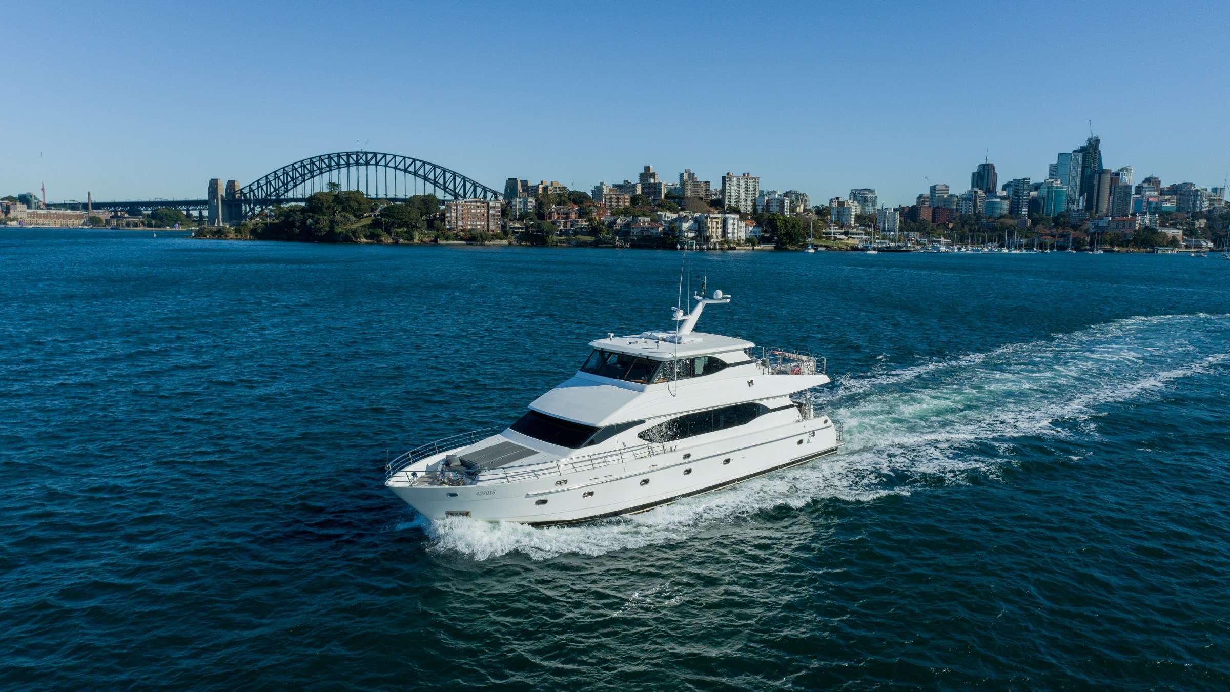 White yacht sailing in front of city skyline and iconic bridge on a clear day.