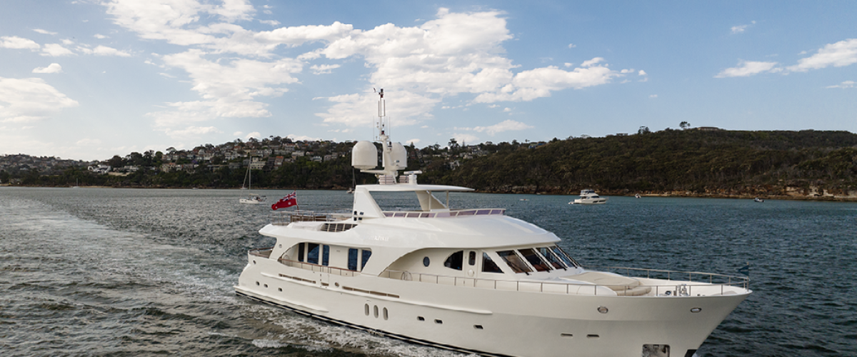 White yacht sailing on a body of water with a hilly shoreline in the background under a partly cloudy sky.