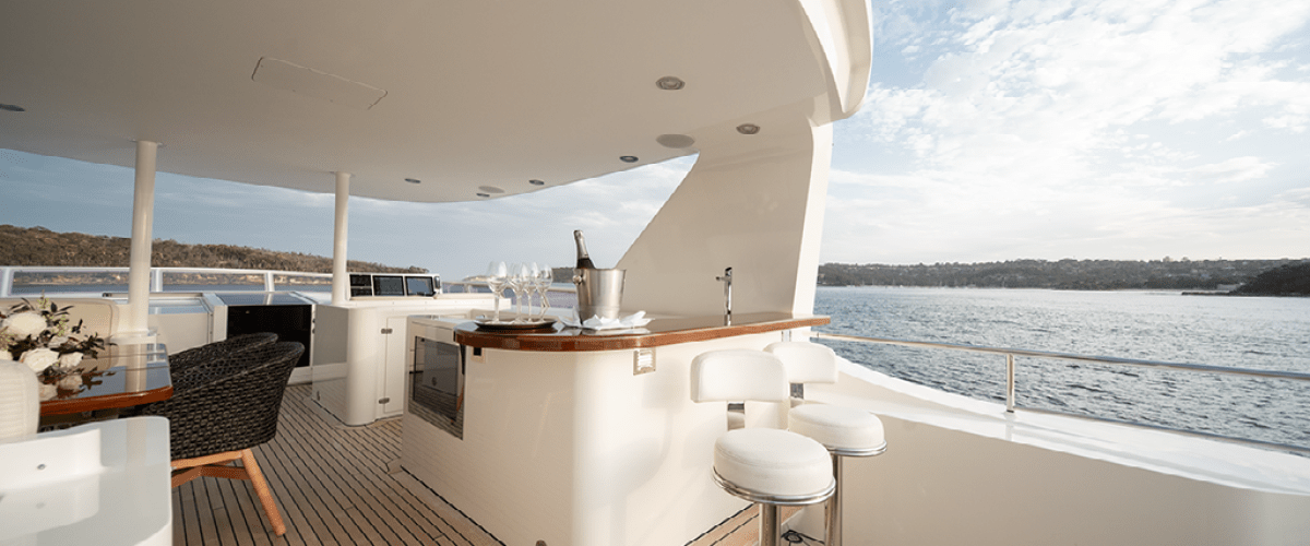 Luxurious yacht deck with bar stools, table, and ocean view under a partly cloudy sky.