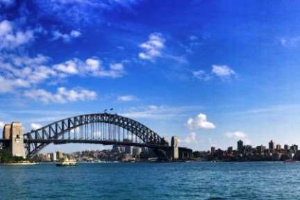 Sydney Harbour Bridge over blue water with scattered clouds in the sky.