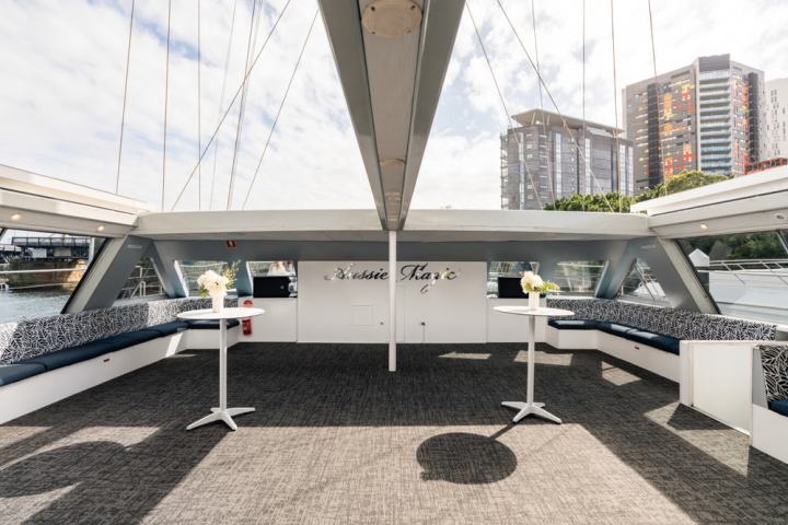 Boat deck with tables, benches, and cityscape view. 'Aussie Magic' sign on wall.