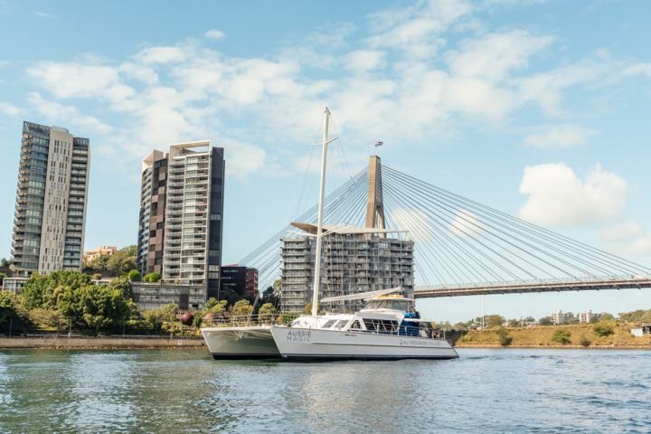 A boat on water with a city skyline and a suspension bridge in the background.