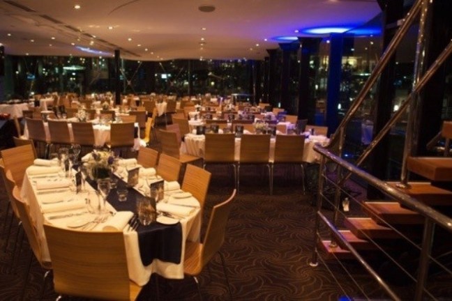 Elegant restaurant with set tables and wooden chairs at night.