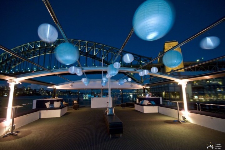 Deck of a boat decorated with blue lanterns, bridge visible at night.