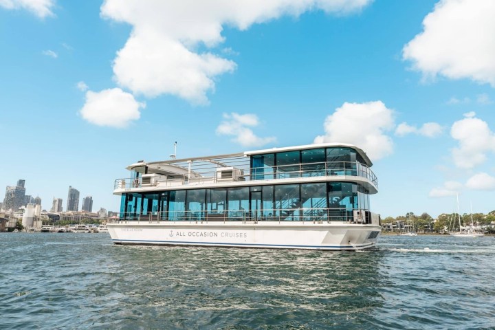 Cruise boat on water with city skyline in background under blue sky.