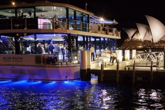 Lit-up boat by dock at night, with city landmark in background.