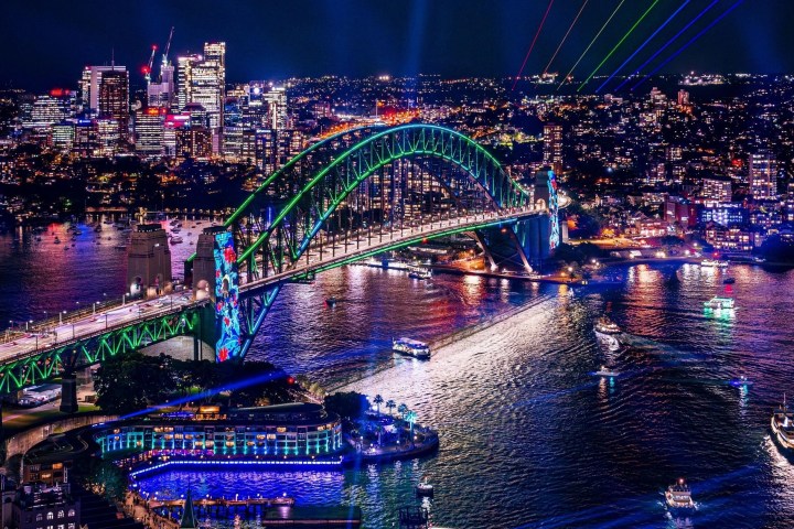 Sydney Harbour Bridge at night with colorful lights and boats in the water.