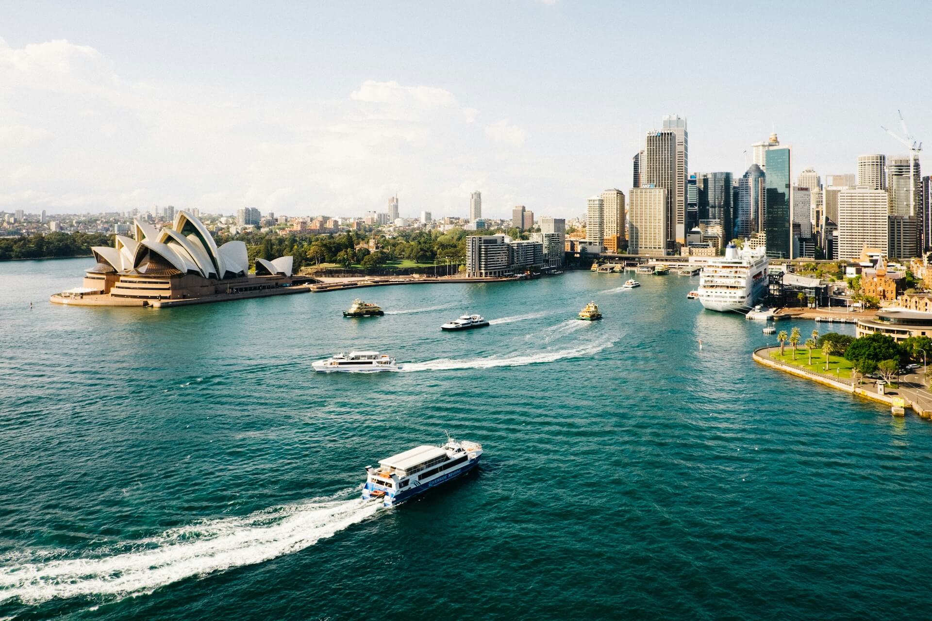Aerial view of Sydney Harbor with boats, opera house, and city skyline.